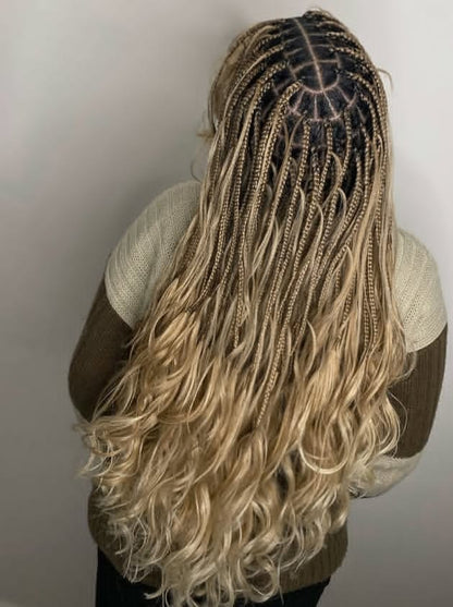Long, wavy blonde hair styled in french curl braids, shown from the back on a person wearing a beige and brown knit sweater against a plain light gray wall.