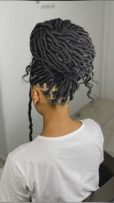 lady with her back facing the camera wearing a white t shirt and individual faux locs put up in a bun
