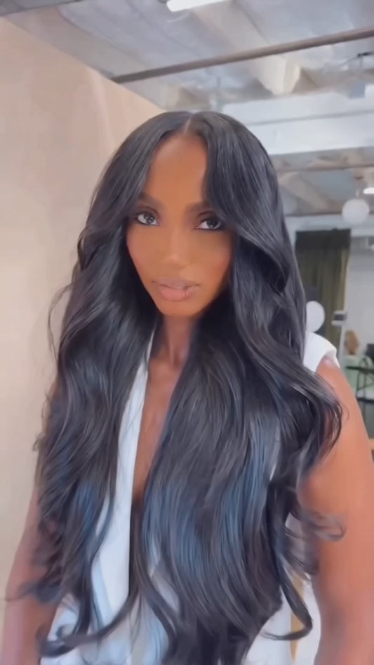 woman in white trousers and matching sleeveless jacket wearing 4 bundles of crown royale hair in 26 inches she wears a 2x6 lace closure behind the hair line with wavy black long hair